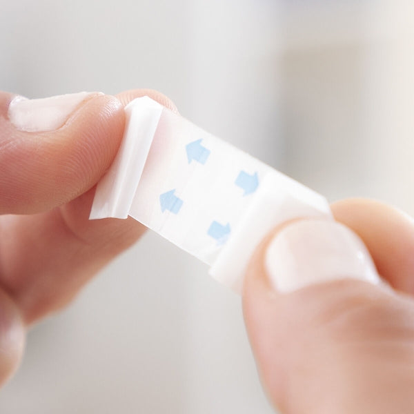 Hand holding a face lifting patches with blue dots on a light background